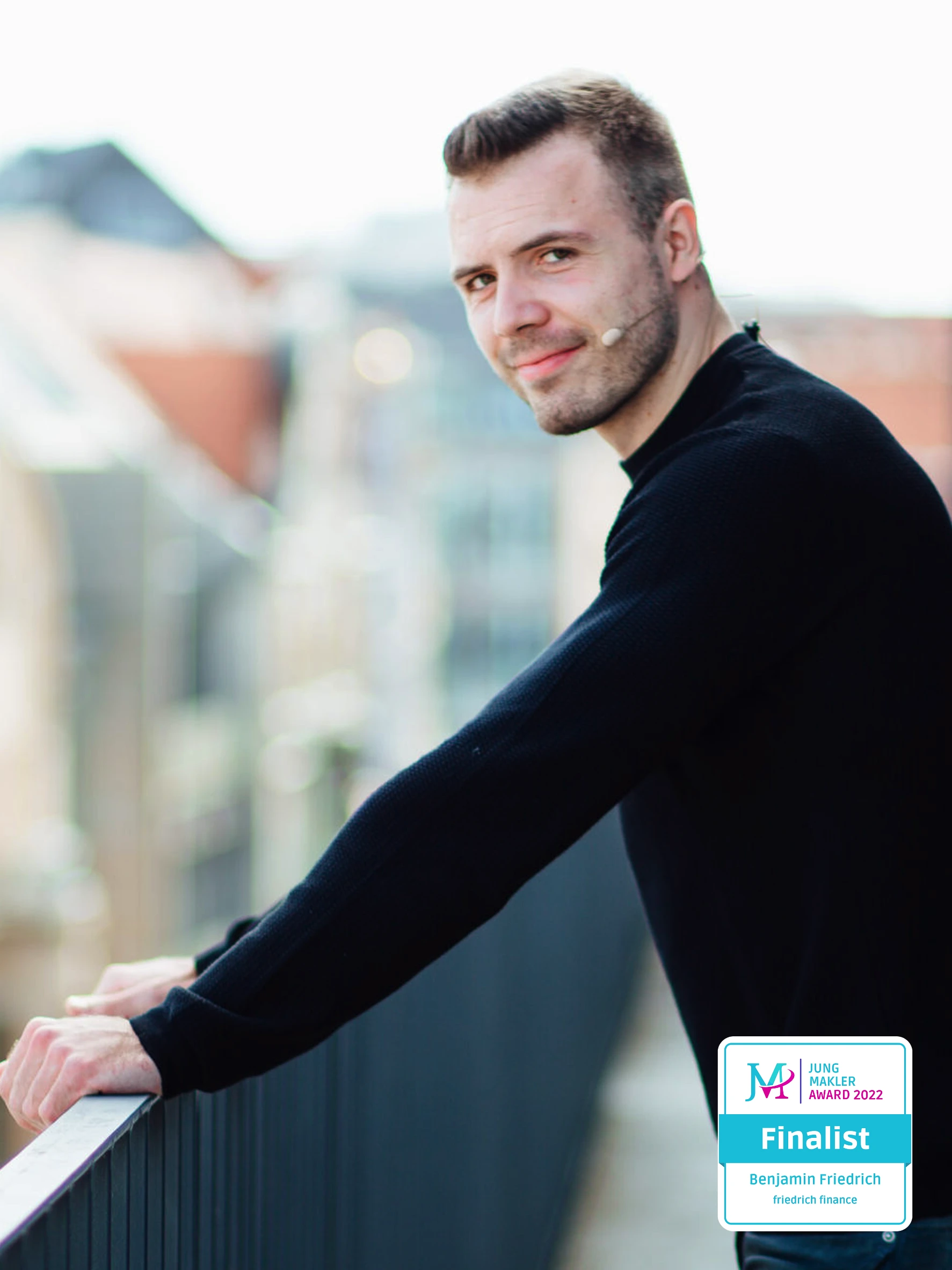 Benjamin Friedrich, Versicherungsberater bei Friedrich Finance, lehnt lächelnd auf einem Balkon mit Stadtblick im Hintergrund.